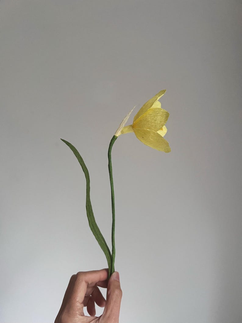 May include: A single yellow paper flower with green paper stems.