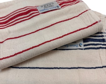 May include: Two folded white cotton kitchen towels with red and blue horizontal stripes. Each towel has a small tag with the brand name "Basic Jewels". The towels are made of a woven fabric.