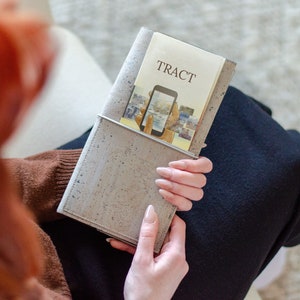 May include: A light gray cork notebook cover with a metal pocket holding a booklet. The booklet has the word "TRACT" printed on the cover and an image of a smartphone. The notebook is held in a person's hands.