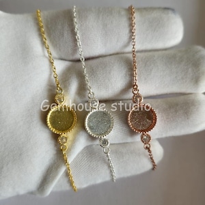 May include: Three delicate bracelets in gold, silver, and rose gold. Each bracelet features a small, round bezel setting with a sparkling accent stone. The bracelets are displayed on a white surface.