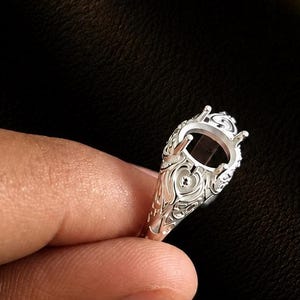 May include: A silver ring setting featuring an intricate filigree design along the band and a pronged head intended for a gemstone. The metal has a polished finish with detailed scrollwork patterns visible on the sides of the ring structure.