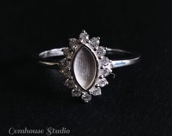 Op de afbeelding: Een zilveren ring met een marquise-vormige zetting omringd door kleine heldere stenen. De ring ligt op een zwarte achtergrond.