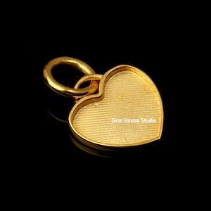 May include: A gold-colored heart-shaped pendant with a textured surface and a loop for attaching to a chain. The pendant has a smooth, polished finish and is set against a black background.