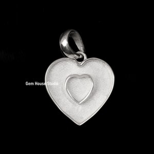 May include: A silver heart pendant with a textured finish, featuring a smaller heart within a larger one. The pendant has a loop for a chain. The image is set against a black background.