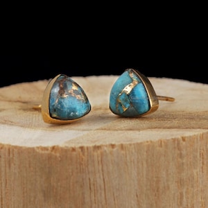 Op de afbeelding: Een paar gouden driehoekige oorbel studs met turquoise en gouden inleg.