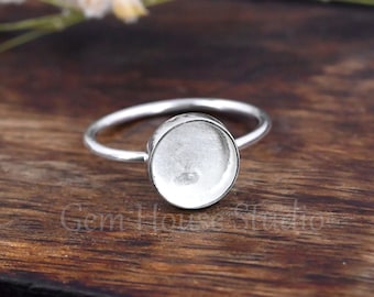 Könnte beinhalten: Ein silberner Ring mit einer runden Fassung für einen Cabochon-Stein. Der Ring liegt auf einer Holzoberfläche.