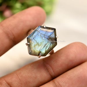 May include: A silver ring with a large, hexagonal, iridescent labradorite gemstone. The stone has a blue, green, and gray color.