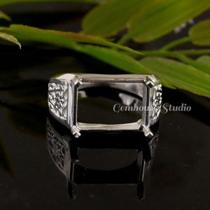 May include: A silver-colored ring setting with an open rectangular space for a gemstone. The ring features ornate floral detailing on the sides and the text "Cemhouse Studio".