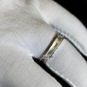Può includere: Primo piano di un anello d'argento. L'anello è sottile e ha un design semplice. L'anello è appoggiato su un tessuto bianco. Il testo "Gem House Studio" è visibile sul tessuto.