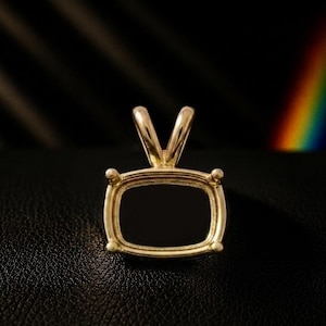 May include: A gold pendant setting featuring a rectangular frame with rounded corners and four prongs at each corner. The center is filled with a smooth, flat, opaque black stone. A polished gold bail is attached to the top for a chain to pass through.