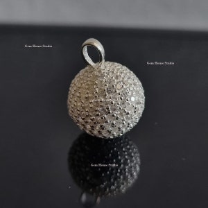 May include: A silver pendant in the shape of a sphere, completely covered in small, clear, sparkling stones. The pendant has a loop at the top for attaching to a chain.
