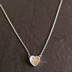 May include: A silver chain necklace with a heart-shaped pendant. The pendant is hollow and has a smooth, polished finish.