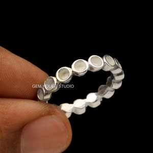 Puede incluir: Anillo de plata con una fila de piedras redondas engastadas en bisel. El anillo está hecho de plata de ley y tiene un acabado pulido.