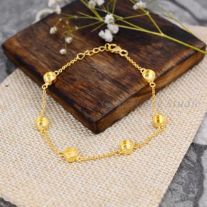 May include: A gold chain bracelet with five round bezels. The bracelet is on a wooden surface.
