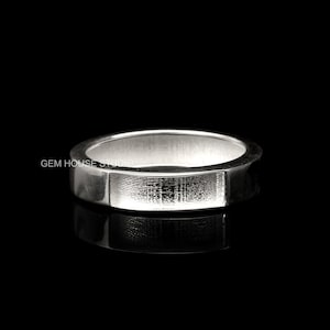 May include: A silver band ring with a textured surface. The ring is thick and has a flat top.