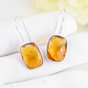 May include: A pair of silver dangle earrings with amber-colored faceted gemstone drops. The earrings have a simple design and are perfect for everyday wear.