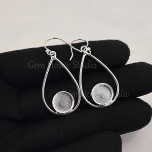 May include: A pair of silver teardrop-shaped earrings with a round, clear glass cabochon in each. The earrings are open at the top and have a hook closure.