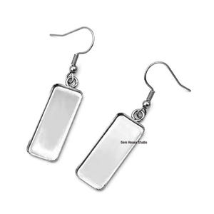 May include: A pair of silver earring blanks with rectangular glass inserts. The earrings are ready to be customized with your own designs.