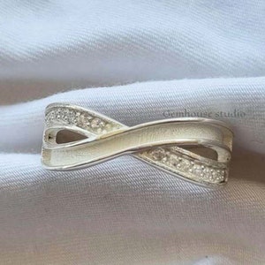 May include: A silver ring with a criss-cross design and small clear stones set in the band.