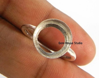 Könnte beinhalten: Ein silberner Ring mit einer kreisförmigen Fassung, ideal für einen Edelstein. Der Ring wird vor einem hautfarbenen Hintergrund gezeigt, mit dem Text "Gem House Studio" sichtbar.