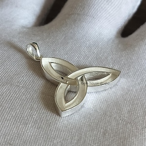 May include: Silver Celtic knot pendant with a three-leaf design. The pendant is on a white surface. "Gem house studio" is written on the pendant.