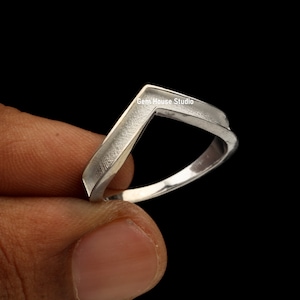 May include: A silver ring with a unique, angular design. The ring is shaped like a V with a flat top and a rounded bottom. The ring is made of polished metal and has a smooth finish.