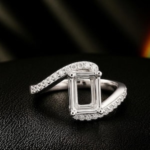 May include: A silver-toned ring featuring a rectangular, empty prong setting at the center. The band has a bypass design with small, clear, round stones embedded along the surface of the metal, creating a sparkling, continuous appearance.
