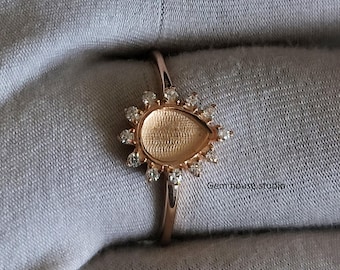 Op de afbeelding: Roségouden ring met een peervormige zetting, omringd door kleine, heldere edelstenen. De ring heeft een slanke band en de zetting is ontworpen om een edelsteen te bevatten. De tekst "Gem house studio" is zichtbaar.