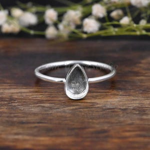 May include: A silver ring with a teardrop-shaped bezel setting. The bezel is empty and ready to be filled with a stone or other material.