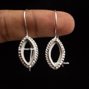 May include: A pair of silver earring blanks with a rope-like design around the edge and a small bead detail. The blanks are oval shaped and have a hook closure. The text "Gem House Studio" is visible on the blanks.