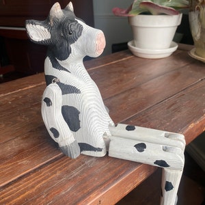 Hand carved wooden cow  with jointed legs sitting on shelf, closeup side profile