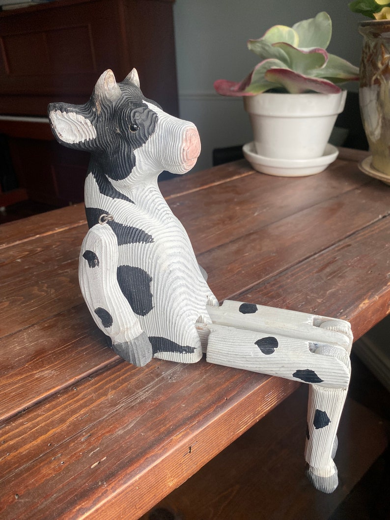 Hand carved wooden cow  with jointed legs sitting on shelf, closeup side profile