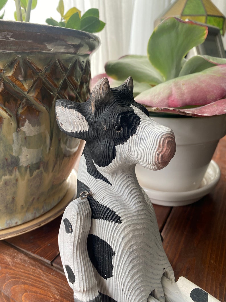 Hand carved wooden cow  with jointed legs sitting on shelf, closeup of face