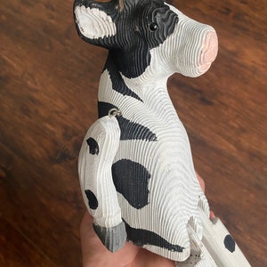 Hand carved wooden cow  with jointed legs sitting on palm of hand