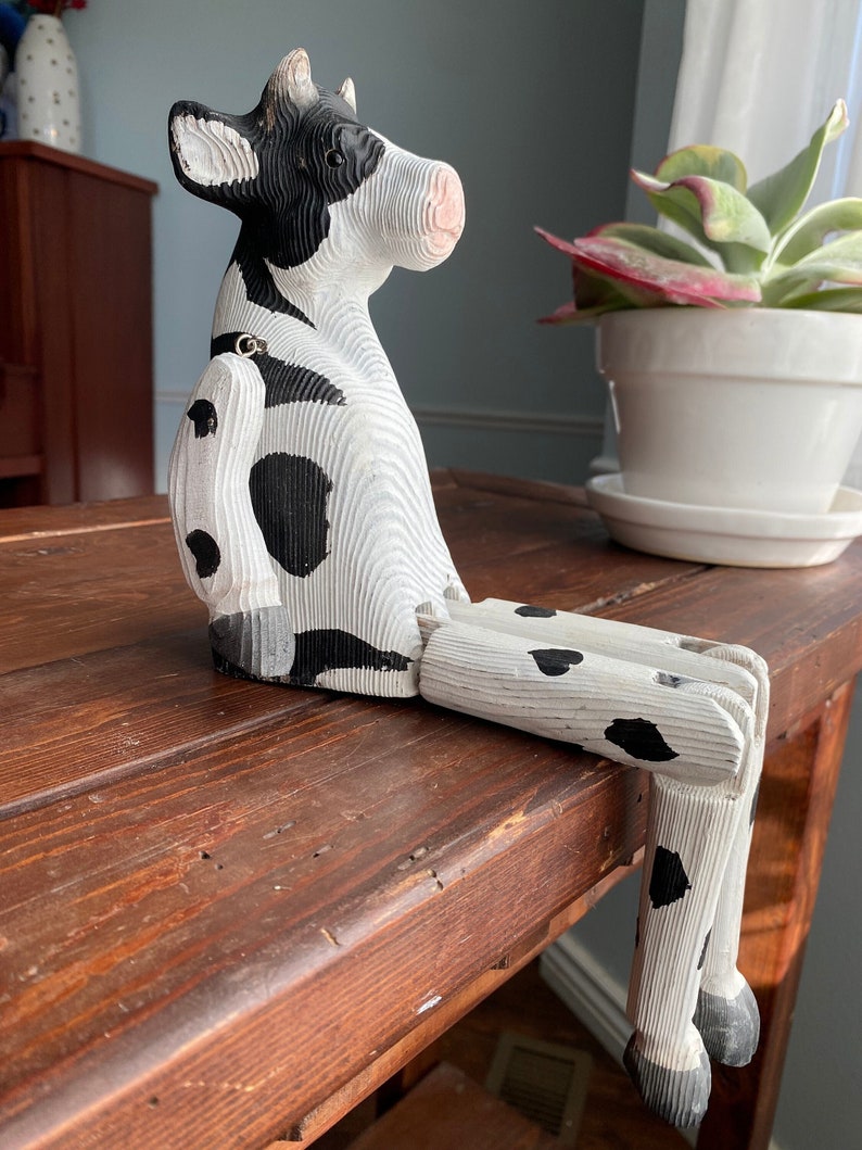 Hand carved wooden cow  with jointed legs sitting on shelf, closeup side profile, slightly below