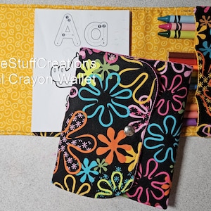 May include: A black travel crayon wallet with a colorful floral design. The wallet is open, revealing crayons and a coloring page with the letter "A". The background is yellow with a swirl pattern. The text "SimpleStuffCreations Travel Crayon Wallet" is visible.
