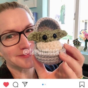 Könnte beinhalten: Ein gehäkeltes Baby Yoda Ornament in hellblau, weiß und grün. Das Ornament wird von einer Person mit einem lächelnden Gesicht gehalten. Der Text "@furonfleek" ist auf dem Bild zu sehen. Die Bildunterschrift lautet "We got this adorable crocheted Baby Yoda Christmas ornament from @furonfleek and I LOVE it show much that it is not going into the bins with the other holidays ornaments! It will live forever by my side in my That's What She Shed next to my tiny succulent. #babyyoda"