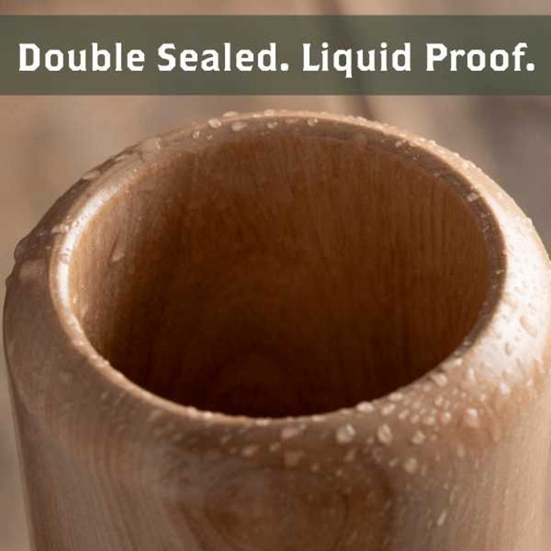 Puede incluir: Primer plano de una taza de madera con un acabado liso de color marr&oacute;n claro. La taza est&aacute; mojada con gotas de agua, lo que indica que es impermeable. El texto "Double Sealed. Liquid Proof." es visible en la parte superior de la imagen.