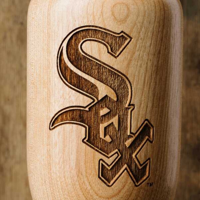 Puede incluir: Un bate de b&eacute;isbol de madera con un logotipo "S" estilizado de color marr&oacute;n oscuro quemado en la superficie. El logotipo es una marca registrada de los Chicago White Sox.