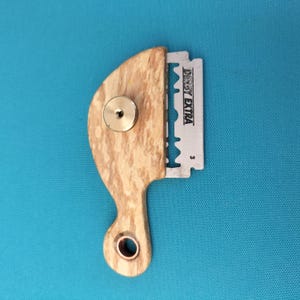 May include: A wooden straight razor handle with a brass fitting and a silver razor blade. The blade is marked "DERBY EXTRA". The handle has a light brown wood grain pattern and a curved design.