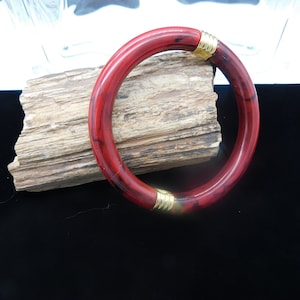 May include: A red and black bangle bracelet with gold accents. The bracelet is made of a smooth, hard plastic.