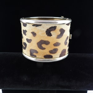 Puede incluir: Un brazalete de metal plateado con estampado de leopardo. El brazalete está hecho de metal y tiene un diseño de estampado de leopardo.