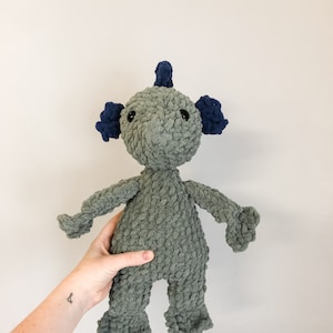 May include: A gray crocheted plush toy with blue ears and a blue topknot. The toy has a textured, fuzzy surface and black eyes.