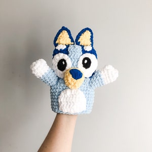 May include: A blue, yellow, and white crocheted puppet of a dog with big eyes. The puppet is designed to fit on a hand.