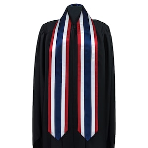 May include: A graduation stole with red, white and blue stripes. The stole is made of satin and is worn over a black graduation gown.