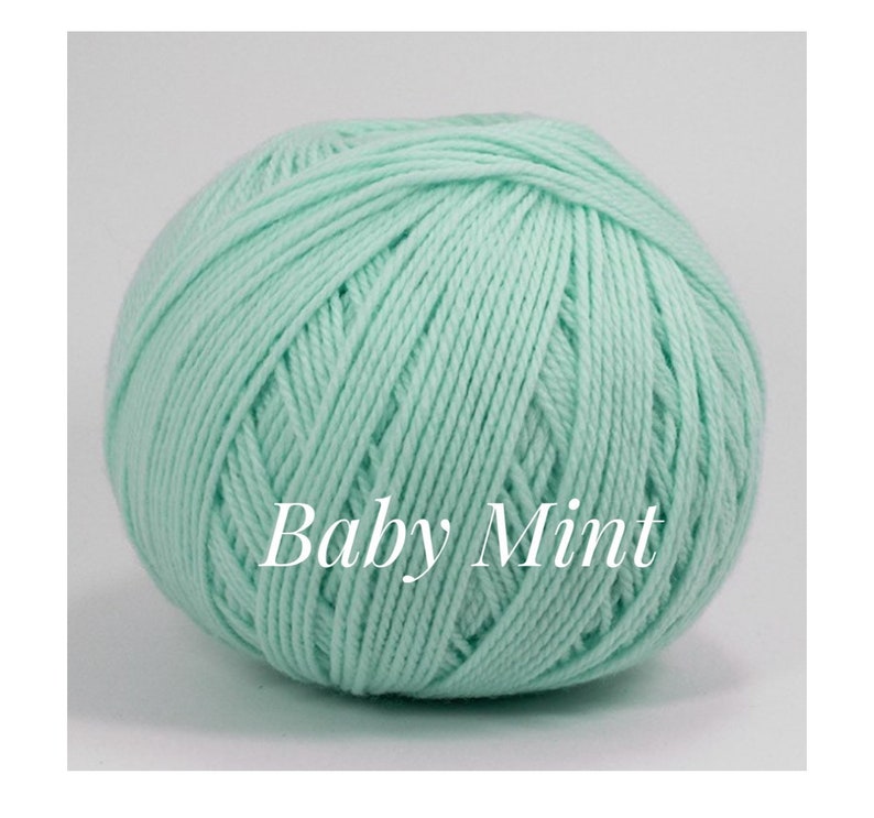 May include: A ball of Baby Mint yarn, a soft, light green color. The yarn is tightly wound, showing the texture of the individual strands. The text "Baby Mint" is printed on the yarn.