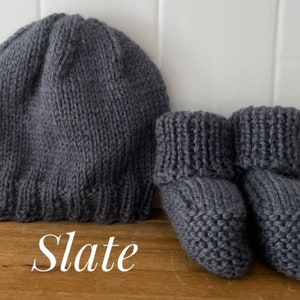 May include: A knitted slate gray baby hat and matching booties. The hat is a simple beanie style, and the booties have a folded cuff. The word "Slate" is written in cursive at the bottom of the image.