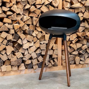 May include: A black metal outdoor fireplace with a rounded design and a wood-burning fire pit. The fireplace is on a stand with three wooden legs.