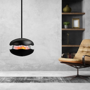 Puede incluir: Una chimenea negra colgante con una llama naranja incandescente en su interior, un sillón de cuero marrón, una lámpara de pie con una pantalla negra y una estantería de madera con un jarrón y un marco de fotos.