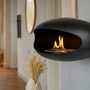 May include: A black, oval-shaped wall-mounted fireplace with a modern design. The fireplace has a glass front and a small flame inside.